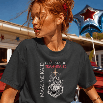A woman wearing a dark charcoal gray graphic t-shirt with the text 'CHALATA HU BRAHMANO' and 'MAAS ME KAID' alongside a snake illustration. The background shows a sunny outdoor setting with a red car and a blue star balloon.