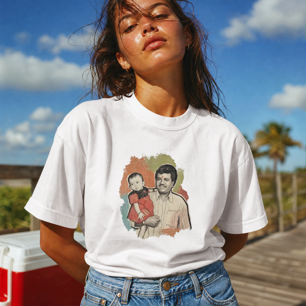 A woman outdoors wearing a white graphic T-shirt with a colorful printed illustration on the front, paired with blue jeans, against a sunny sky and wooden boardwalk background.